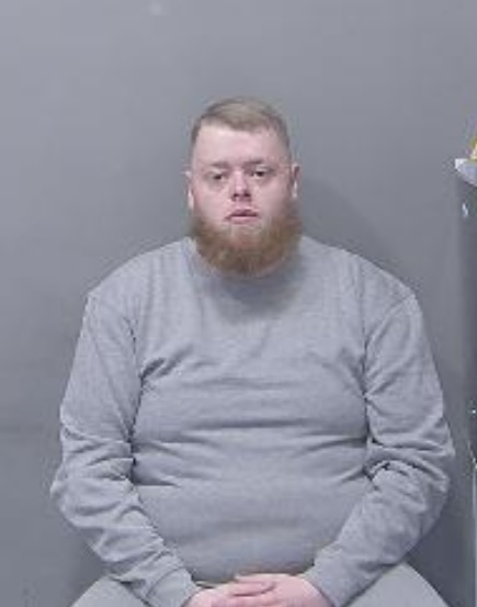Custody image of Tyler McQuarrie, wearing a grey sweatshirt, and he has a ginger beard.
